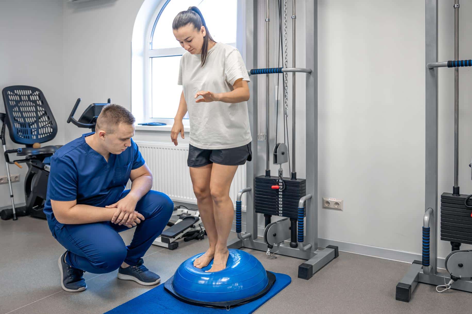 Fisioterapista assiste paziente durante esercizi di equilibrio su bosu ball in palestra riabilitativa per recupero post-chirurgico
